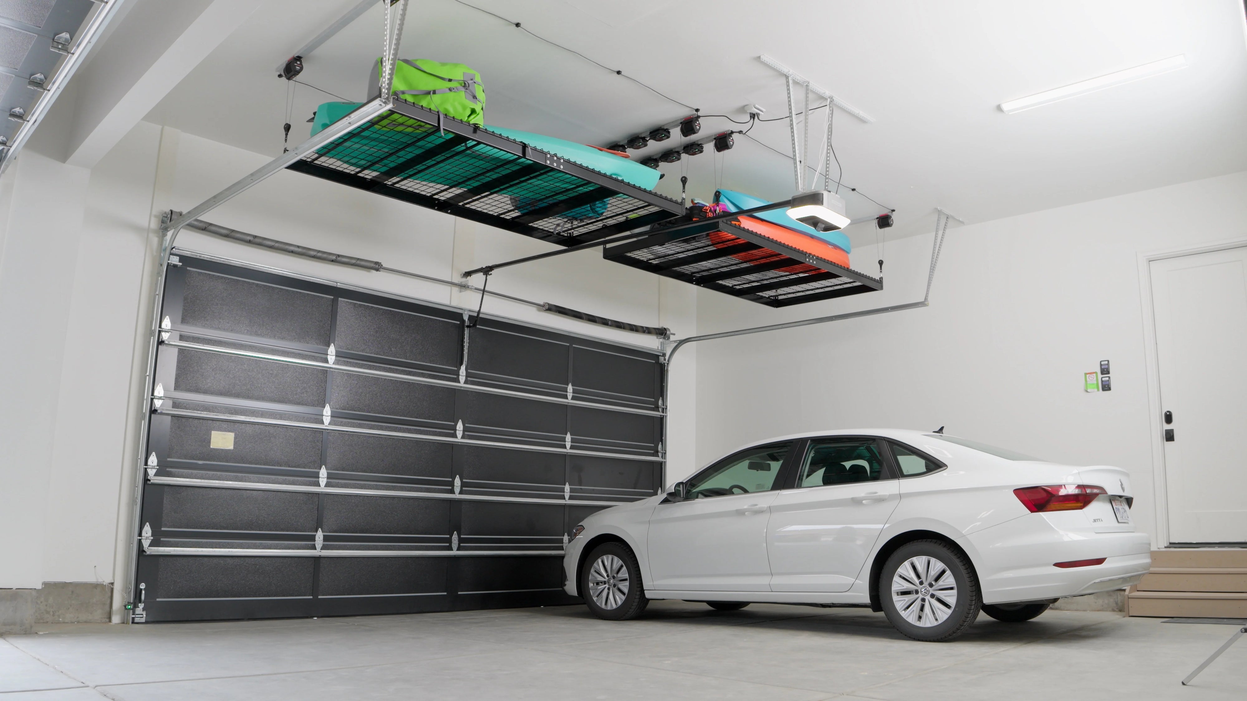 A white car is parked in a garage with a shelf above it.